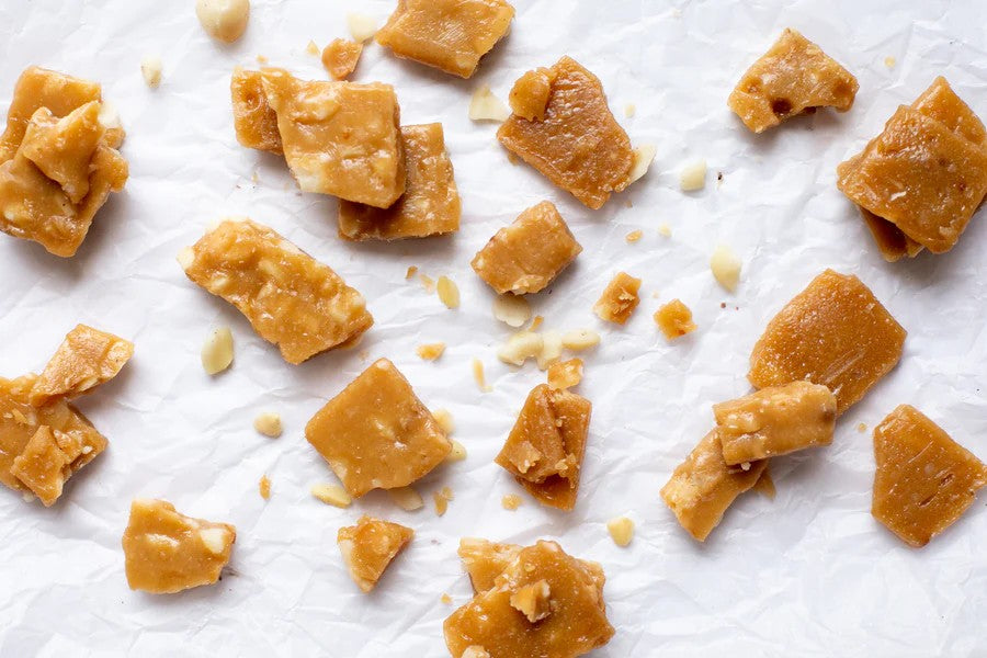 Caramel with macadamia brittles in pieces on a white surface photo from Nutworks