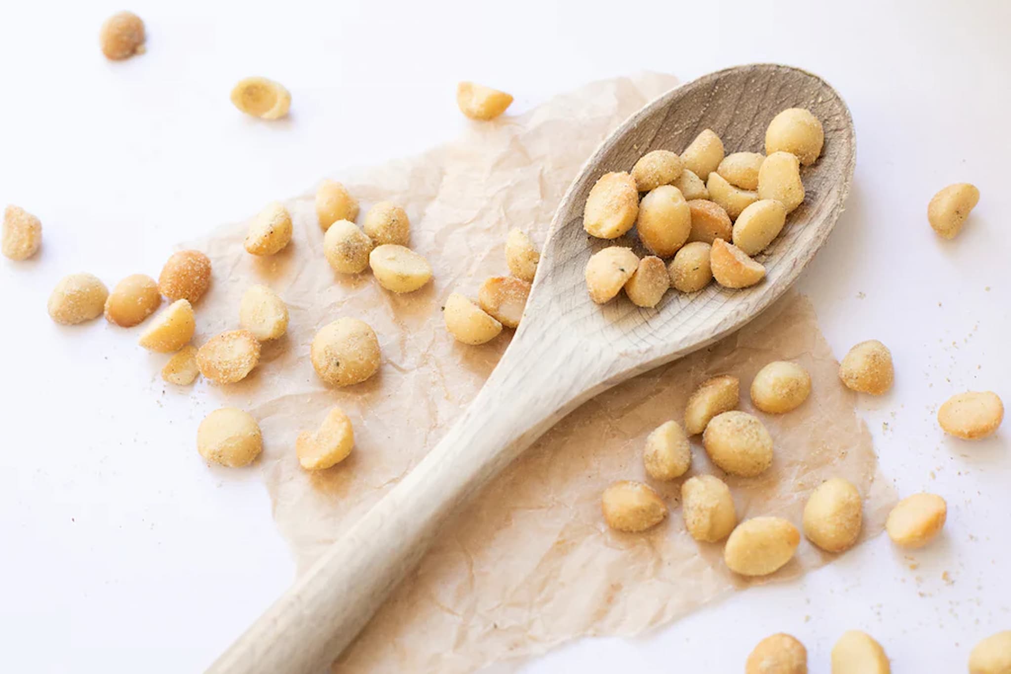 A wooden spoon filled with flavoured premium Australian rosemary and sea salt macadamias on a light background.