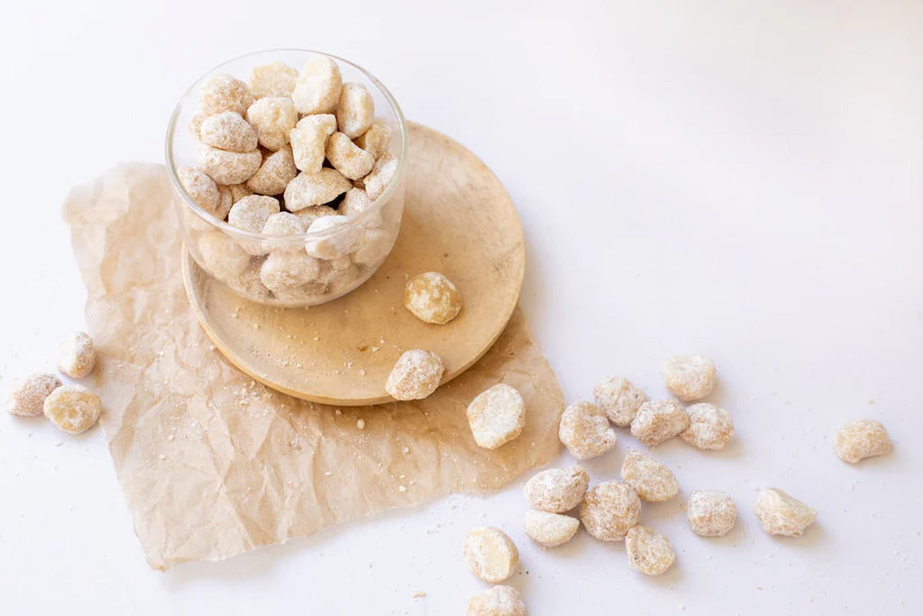 A glass container with butter candy macadamia nuts on a wooden plate on a white background photo from Nutworks.