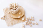 A glass container with butter candy macadamia nuts on a wooden plate on a white background photo from Nutworks.