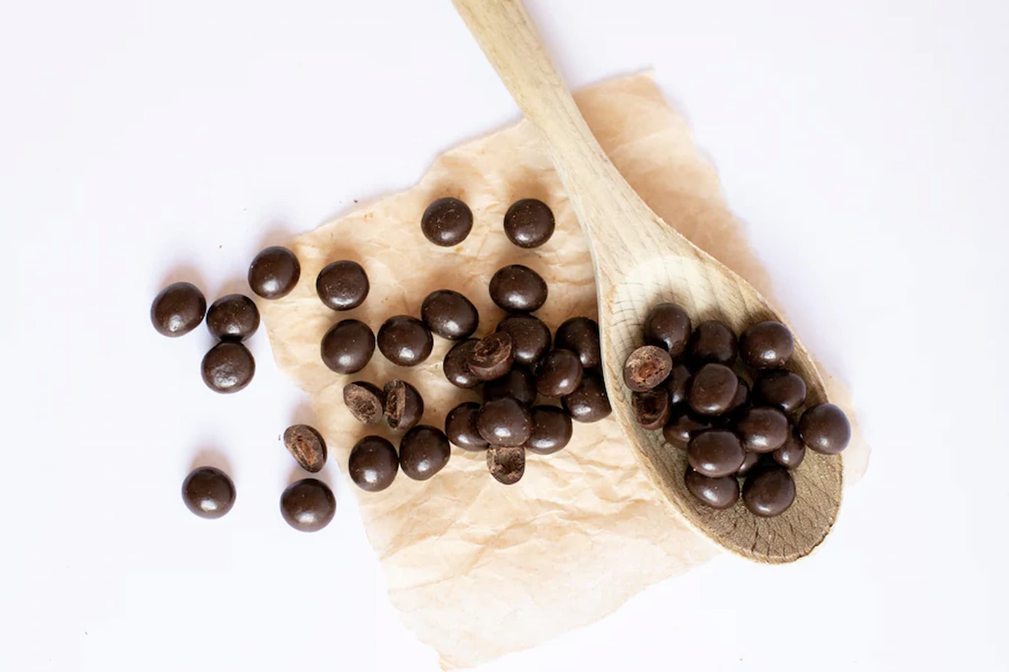 Wooden spoon filled with dark chocolate balls on a white background photo from Nutworks