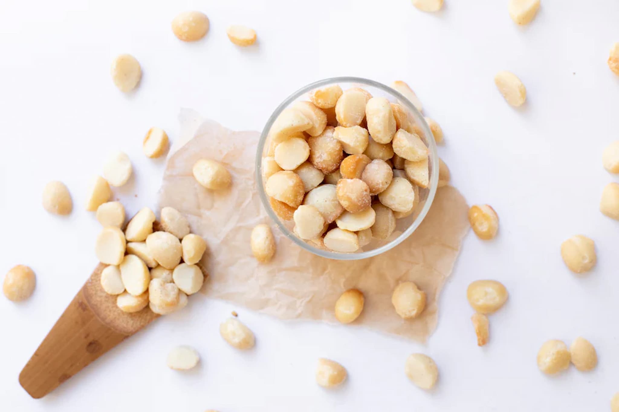 Macadamia nuts in a glass bowl and wooden scoop on a white background photo from Nutworks.