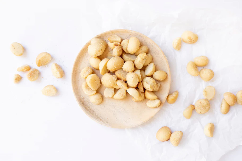 Macadamia roast garlic nuts on a wooden plate with scattered nuts on a white background photo from Nutworks