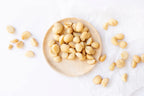 Macadamia roast garlic nuts on a wooden plate with scattered nuts on a white background photo from Nutworks