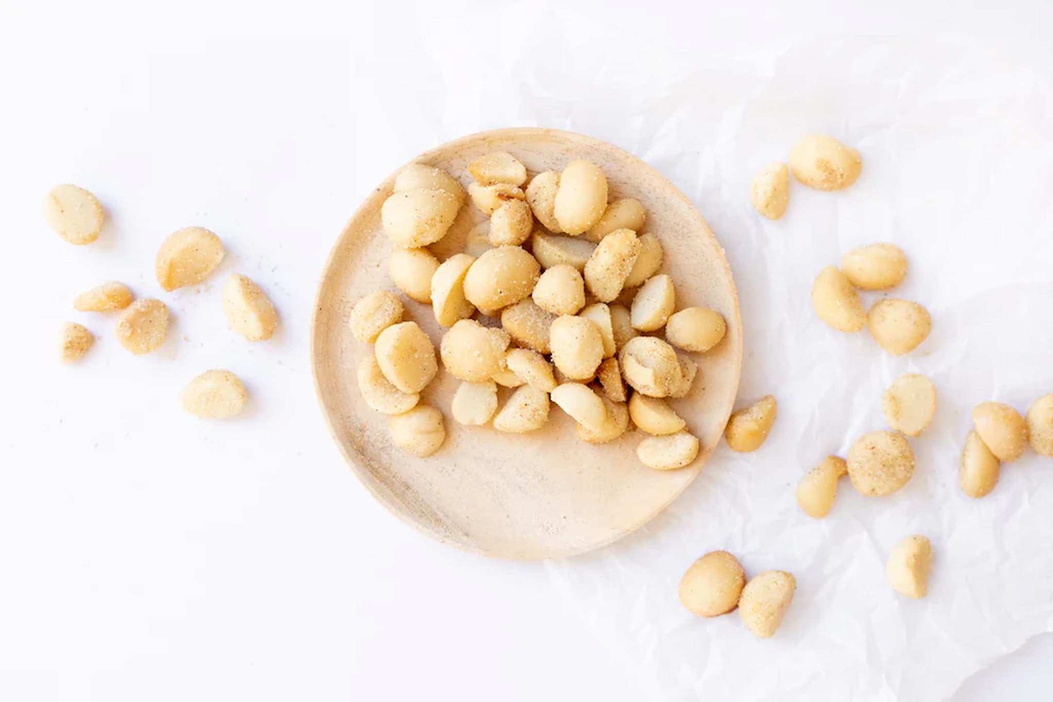 Macadamia roast garlic nuts on a wooden plate with scattered nuts on a white background photo from Nutworks