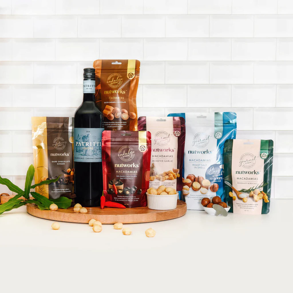 Assorted macadamia nut packages and a bottle of wine on a wooden board with a white tiled background photo from Nutworks.