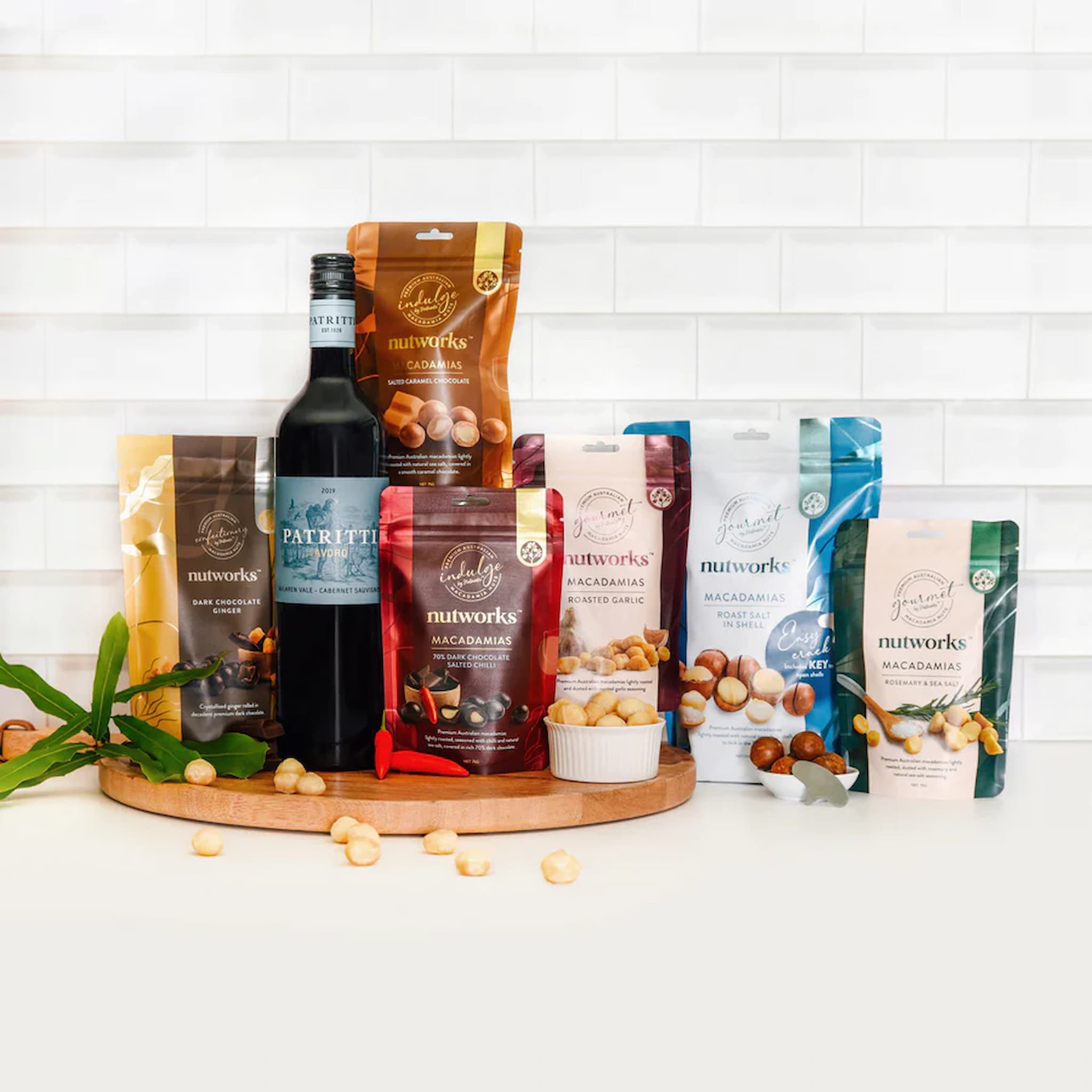 Assorted macadamia nut packages and a bottle of wine on a wooden board with a white tiled background photo from Nutworks.