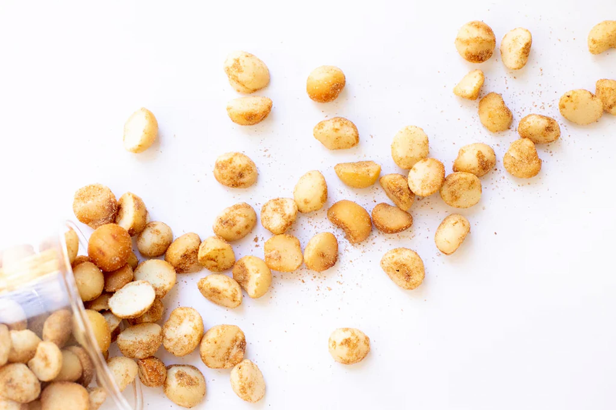 wasabi premium Australian Macadamia nuts scattered on a white surface with a small container of nuts.