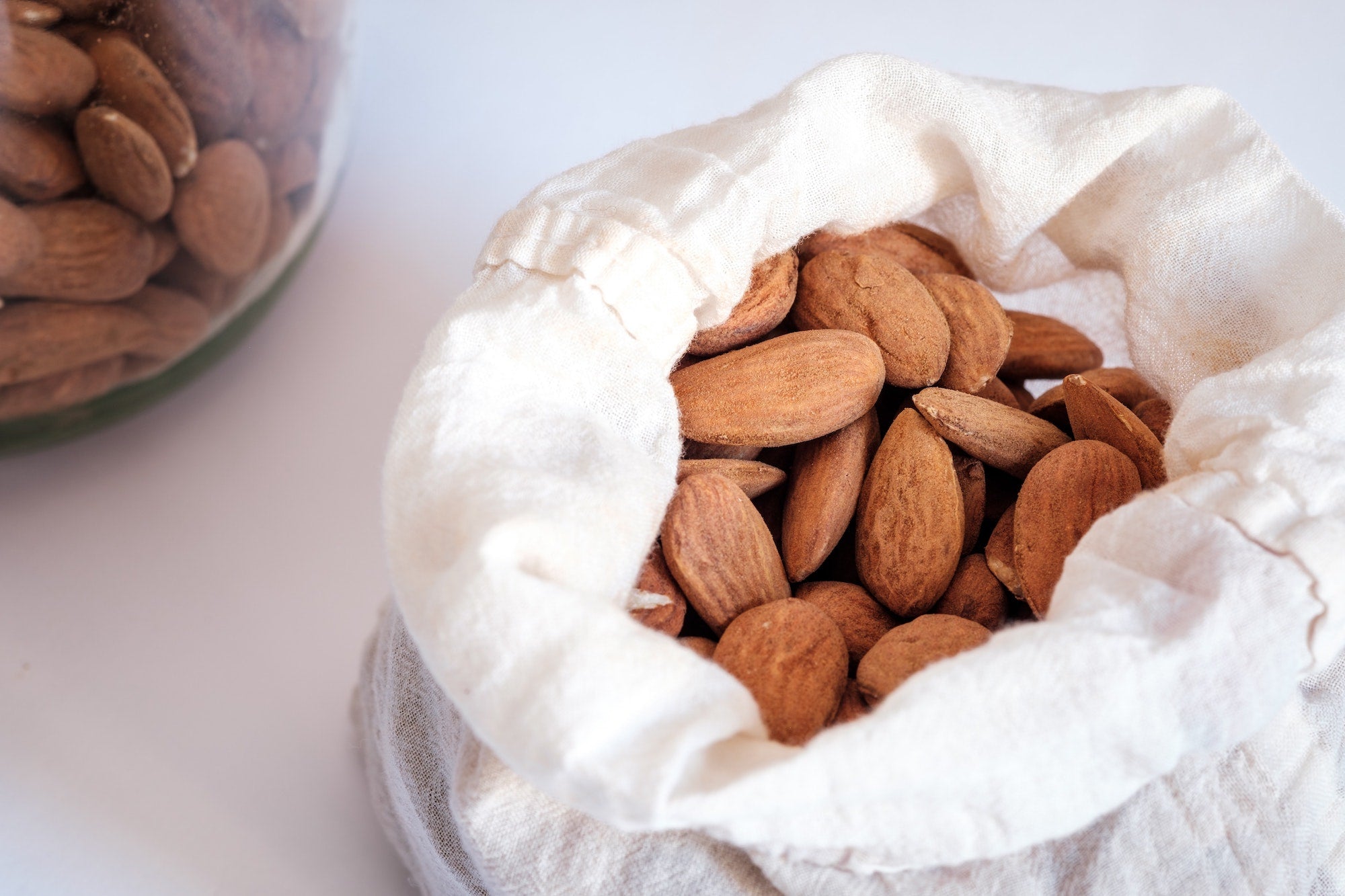 A cloth bag filled with dry roasted almonds, with a few almonds scattered outside the bag from Nutworks