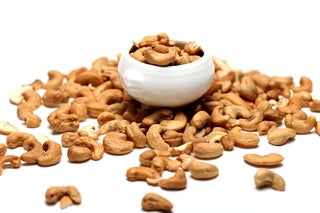A pile of raw cashew nuts scattered around a small white bowl photo from Nutworks.